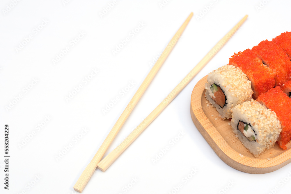 Delicious Japanese rolls with salmon, avocado, cucumber, cheese on wooden plate with wood sticks with selective focus on white background. Asian food concept. Healthy eating Delicious Japanese rolls with salmon, avocado, cucumber, cheese on wooden plate with wood sticks with selective focus on white background. Asian food concept. Healthy eating