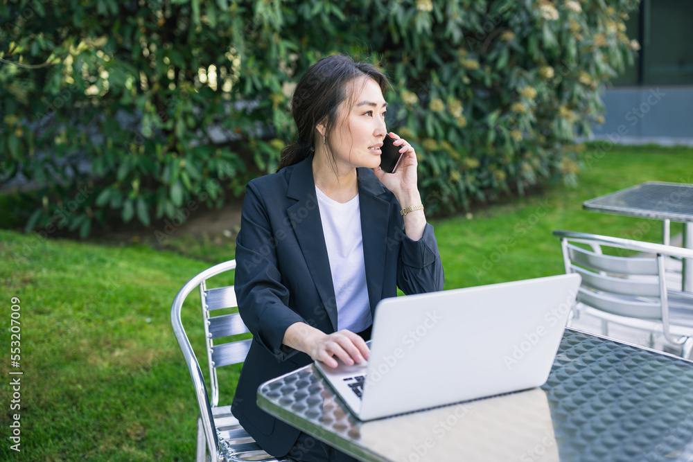 Asian business woman talking on phone and working with laptop outdoor Asian business woman talking on phone and working with laptop outdoor