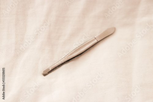 Closeup of a pair of silver tweezers laying isolated on white fabric background