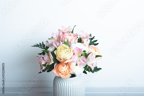 Beautiful bouquet of fresh colorful pastel ranunculus and lily flowers in full bloom with green fern leaves in vase against white background, close up. Negative space.
