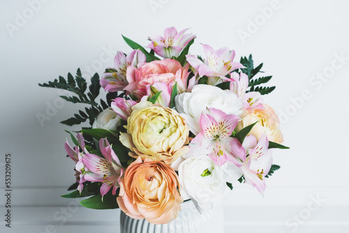 Beautiful bouquet of fresh colorful pastel ranunculus and lily flowers in full bloom with green fern leaves in vase against white background  close up. Spring bunch of blossoms.