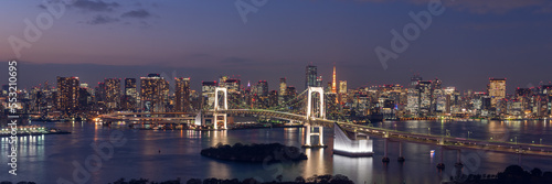 Wide panorama image of Tokyo cityscape at dusk with Rainbow bridge and Tokyo tower.