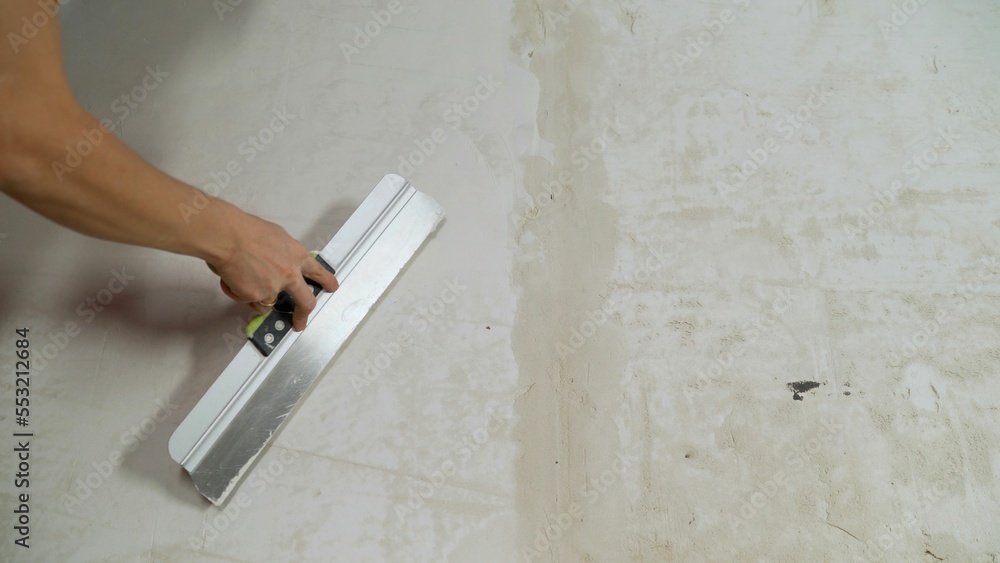 Master's hands apply the finishing putty on the concrete wall, close-up, there is a place for the inscription. Hand with a spatula to apply putty on the wall. Master's hands apply the finishing putty on the concrete wall, close-up, there is a place for the inscription. Hand with a spatula to apply putty on the wall.