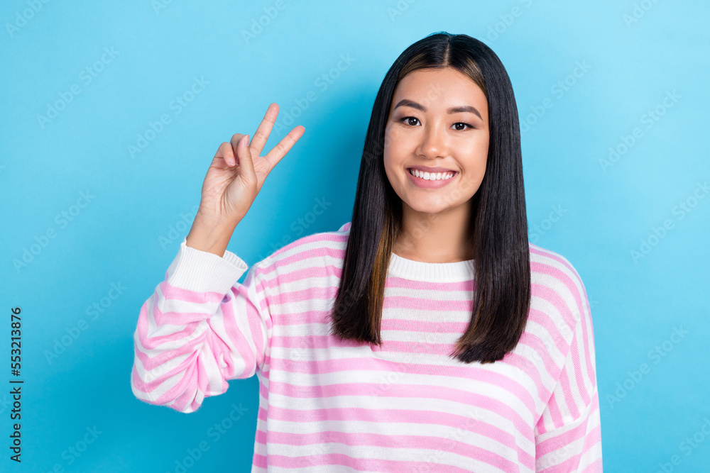 Photo of cheerful funny girl dressed pink pullover smiling showing v-sign isolated blue color background Photo of cheerful funny girl dressed pink pullover smiling showing v-sign isolated blue color background