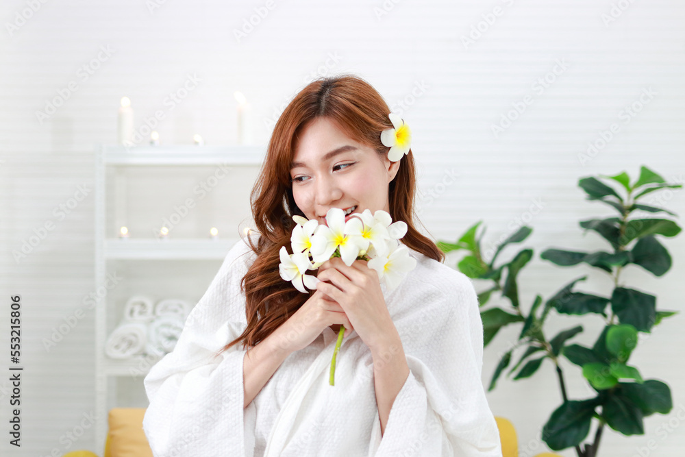 Portrait of a beautiful Asian woman doing a spa at home smiling happily. Dressed in white, standing holding flowers. Asian beauty concept Portrait of a beautiful Asian woman doing a spa at home smiling happily. Dressed in white, standing holding flowers. Asian beauty concept