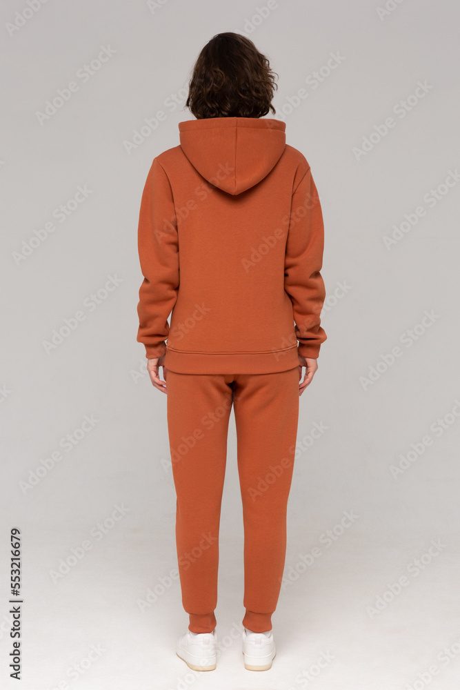 Woman with thick curly hair in a brown suit of hoodies and sweatpants. Shot from the back. Mock-up.