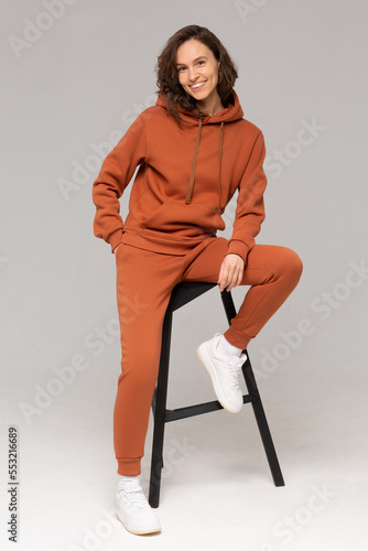Smiling woman with thick curly hair in a brown suit of hoodies and sweatpants. Mock-up.
