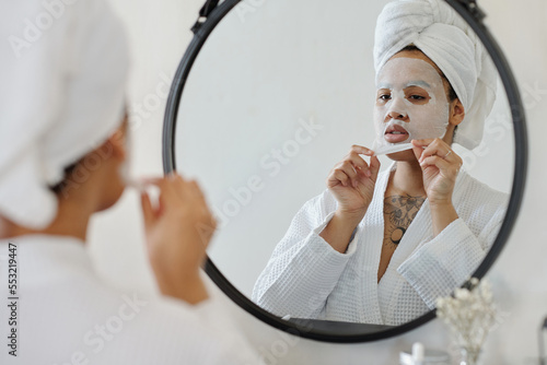 Billede på lærred Young African American woman in white bathrobe and with towel on head taking hyd