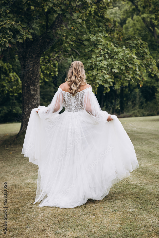 Wedding. A bride in a white dress walks along the green grass against the background of trees
