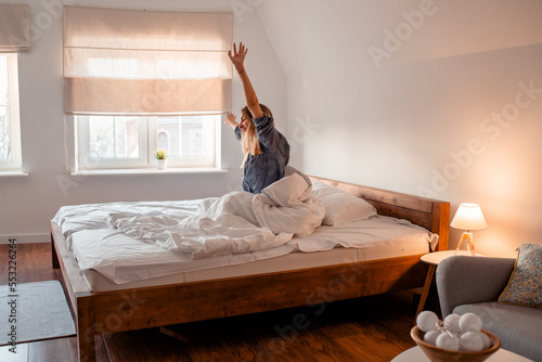 Billede på lærred A girl in pajamas stretches after getting out of bed and looking out the window