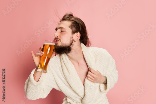 Billede på lærred Portrait of emotive funny man in bathrobe posing with glass of lager beer isolated on pink background