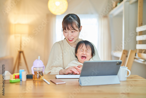 自宅でタブレットPCを操作する女性と泣く幼児