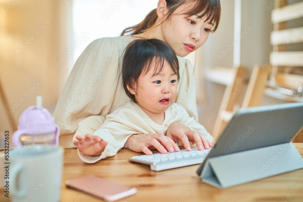 自宅でタブレットPCを操作する女性と泣く幼児 自宅でタブレットPCを操作する女性と泣く幼児