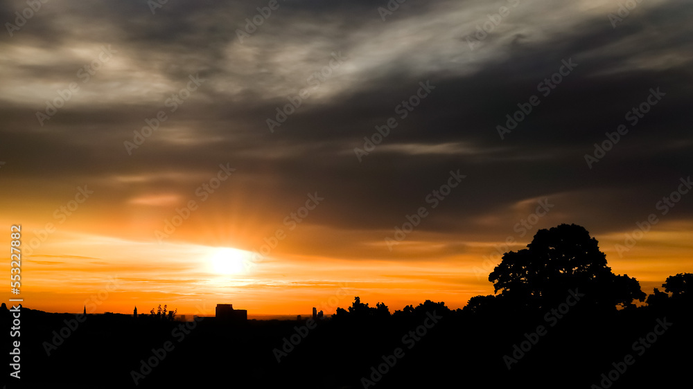 Dramatic storm clouds and sunrise with tree silhouettes in London