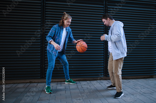Man with down syndrome playing basketball outdoor with his friend. Concept of friendship and integration people with disability into society.