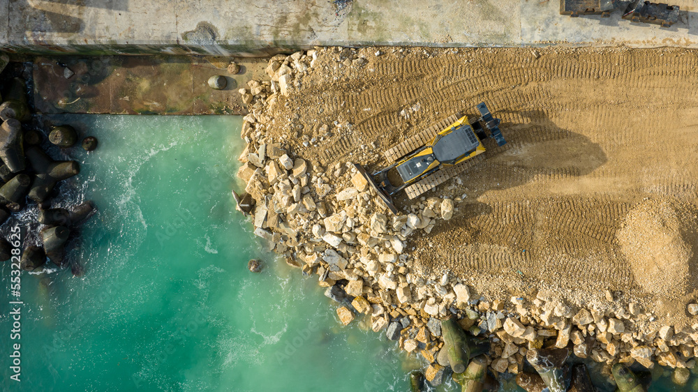 Aerial view of waterfront construction site with excavator. Bulldozer working on a breakwater construction - obrazy, fototapety, plakaty 