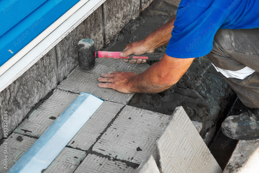 Professional bricklayer lays tiles. Hands of builder close-up with hammer. Repair of stone scaffolding of building. Construction contractor at work. Real workflow..