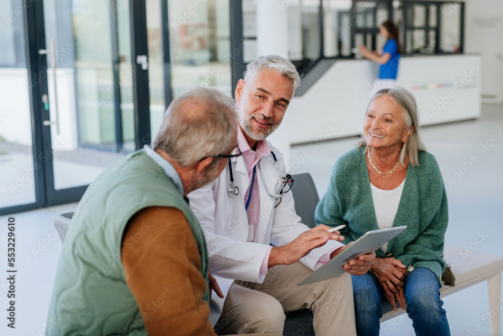 Obraz premium Mature doctor talking with his senior patients at hospital corridor.