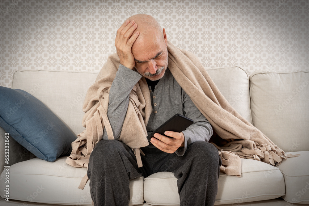 Serious Sad Old Man Sitting with Blanket on Shoulders with Mobile Phone in Hand