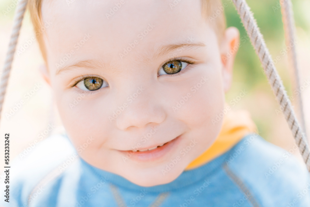 Сlose-up portrait of a cute green-eyed boy of three years looking with interest and smiling - obrazy, fototapety, plakaty 