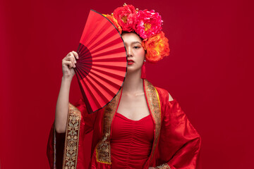 Young asian woman wearing qipao cheongsam dress with Chinese folding fan on red background for Chinese new year festival
