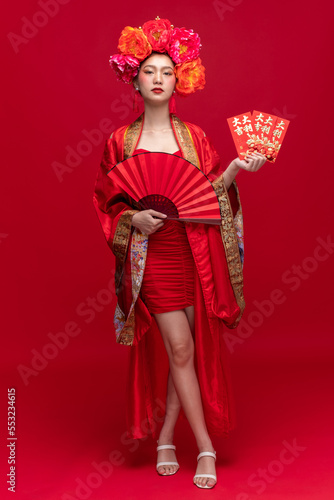 Full body portrait of young asian woman wearing fashion modern qipao cheongsam dress smile and flower on head on red background for Chinese new year festival