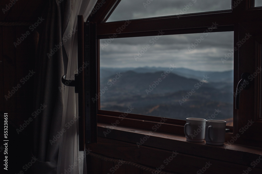 Fototapeta premium Two cups of tea on windowsill with opened window in front of mountains view