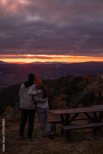 Young couple from behind enjoying fall mountains landscape in the evening