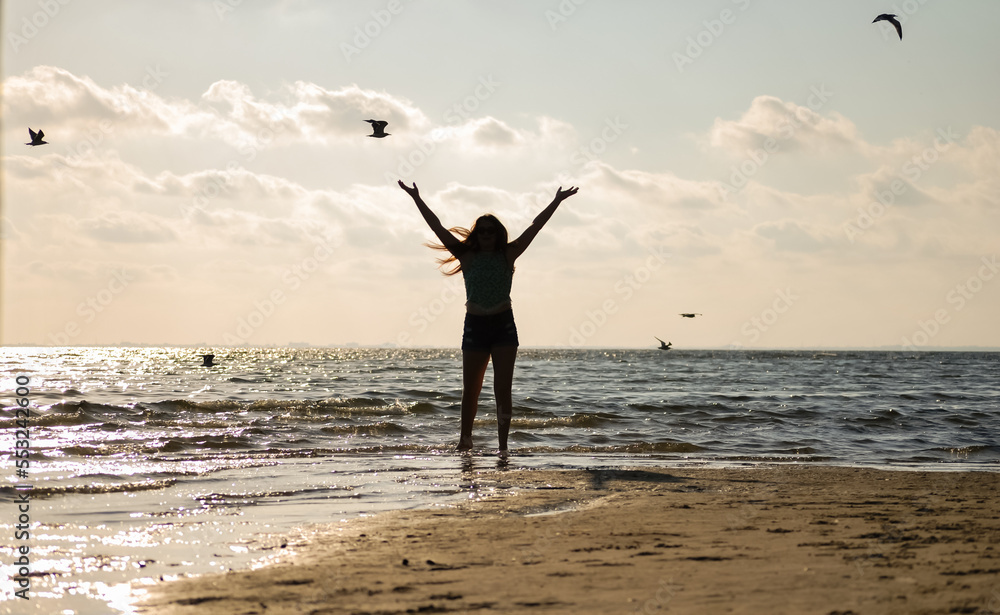 girl playing on the beach with her arms in the air reaching for the sky ...