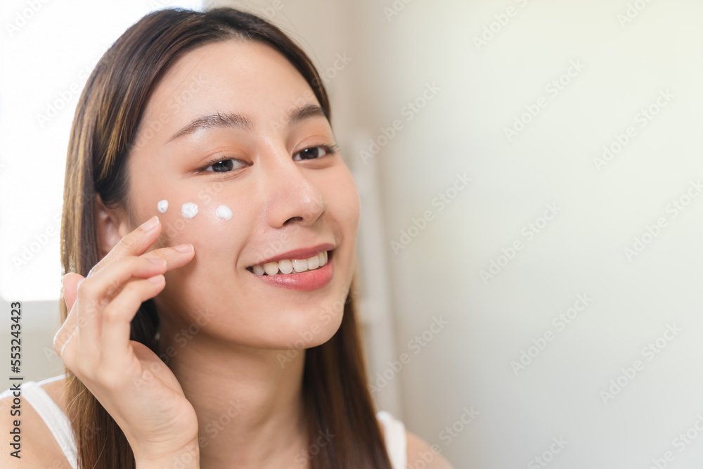 Asian young woman applying cream to her face in routine self care. Asian young woman applying cream to her face in routine self care.