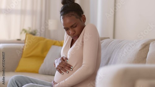 Pregnancy problems. Young unhappy pregnant african american woman suffering from painful feeling, touching her belly