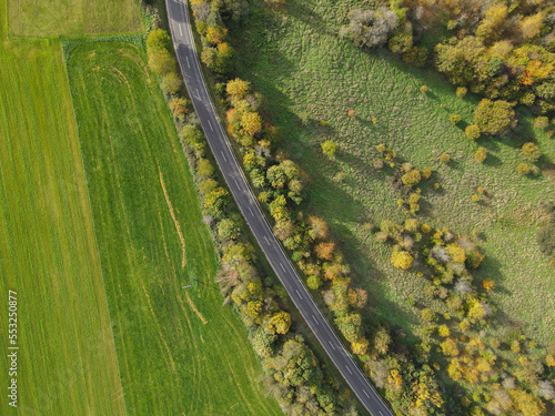 View from above of a road between grassland and trees on a sunny autumn day