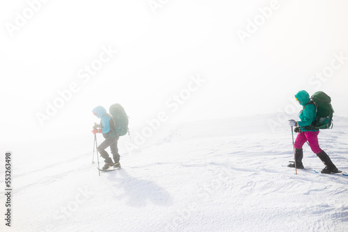 two girls with a backpack and snowshoes walk in the snow during a snow storm.