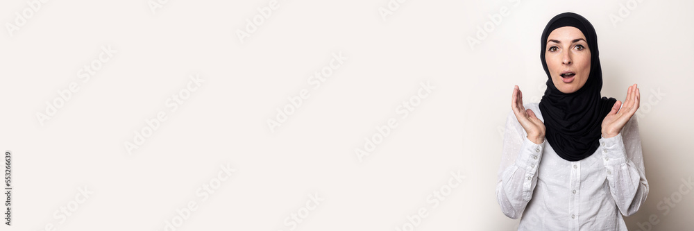 Young woman with surprised face in white shirt and hijab on light background Young woman with surprised face in white shirt and hijab on light background