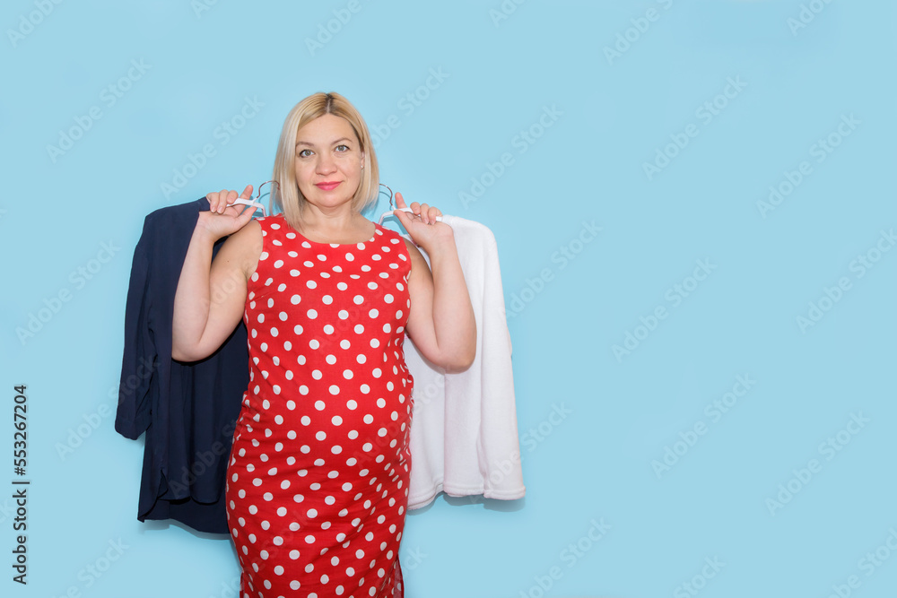 pregnant woman holding clothes on hangers in her hands on a blue background with copy space pregnant woman holding clothes on hangers in her hands on a blue background with copy space