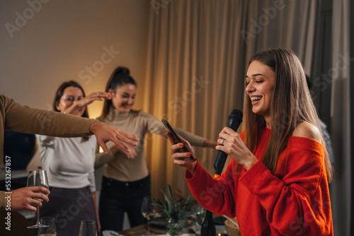 Woman sings in the microphone at a house party, friends dance