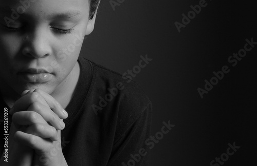 Photography little boy praying to God with hands together on black background with people st