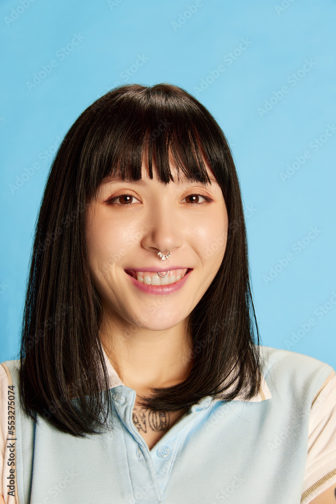 Close-up portrait of young emotive woman with piercing posing isolated over blue background. Cheerfully smiling Close-up portrait of young emotive woman with piercing posing isolated over blue background. Cheerfully smiling