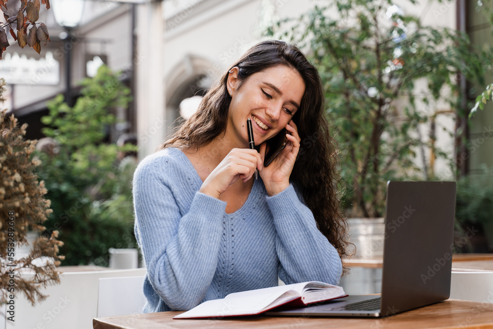 Cheerful girl with phone and laptop is working online with customers and chatting with team. Busy business woman with laptop and phone is chatting and working remotely with colleagues. Cheerful girl with phone and laptop is working online with customers and chatting with team. Busy business woman with laptop and phone is chatting and working remotely with colleagues.