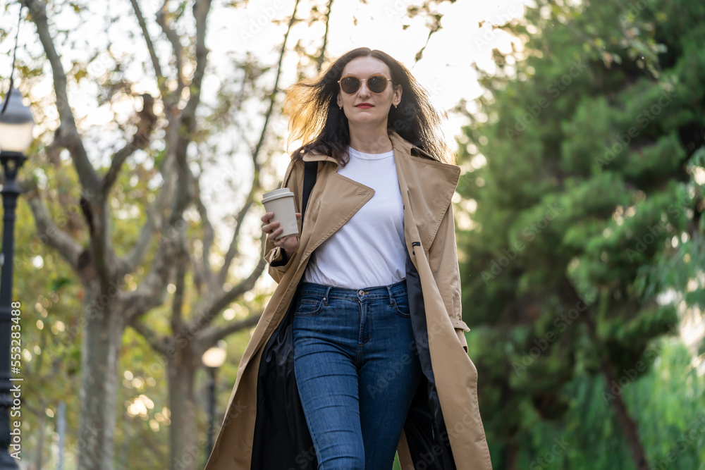 Adult 35s years old businesswoman with long hair, sunglasses and trench coat walk from office to a town with coffee cup. Urban scene of Barcelona city. Adult 35s years old businesswoman with long hair, sunglasses and trench coat walk from office to a town with coffee cup. Urban scene of Barcelona city.