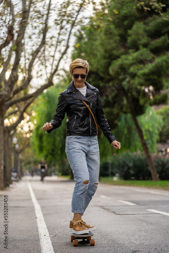 Adult woman with short hair and leather jacket learn to ride skateboard in a city. Urban lifestyle scene in Barcelona. © Zkolra