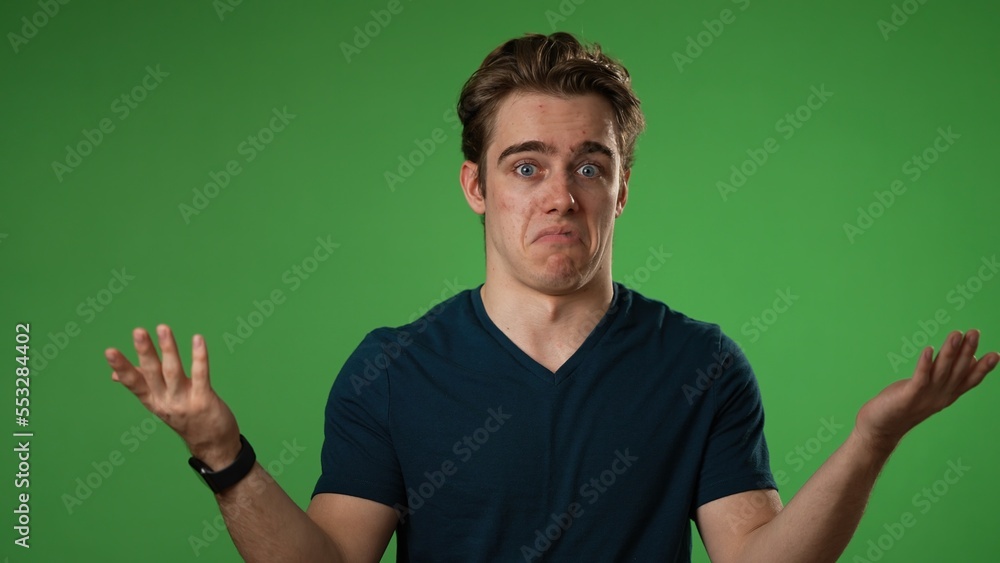 Naklejka premium Portrait of happy young man 20s shrugging shoulders and gesturing I do not know isolated on green screen background 