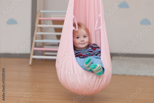 cute little boy in child cocoon hammock at home or kindergarden. toddler or kid in festive room. portrait