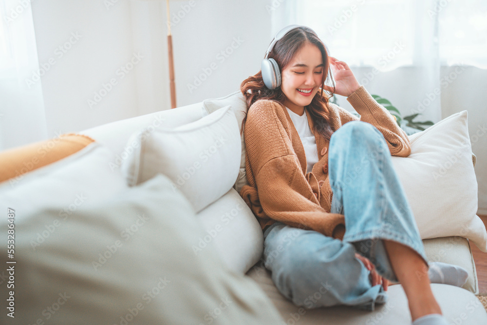 Fototapeta premium Happy woman relaxing in her sofa at home, Smiling girl is listening to music with headphones and lying down with eyes closed, Enjoy good quality sound, Stress free concept.