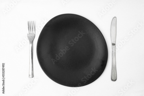 irregular round black plate with silver fork and knife on white