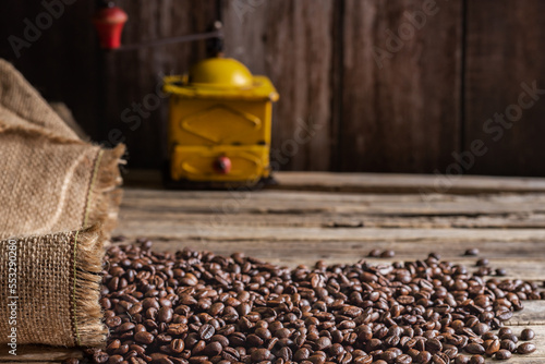 Obraz na płótnie Roasted coffee beans coming out of a sack on a wooden table and in the background an old grinder for grinding coffee. w salonie