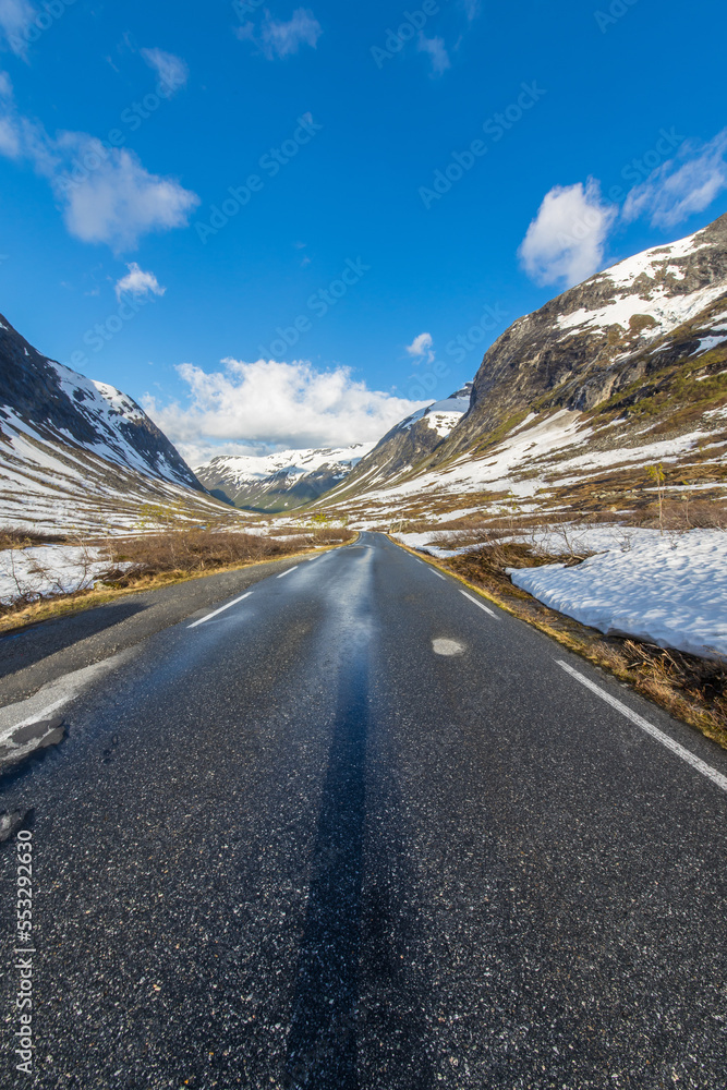 epic mountain pass road to Trollstigen in the morning with snow covered mountains and blue sky