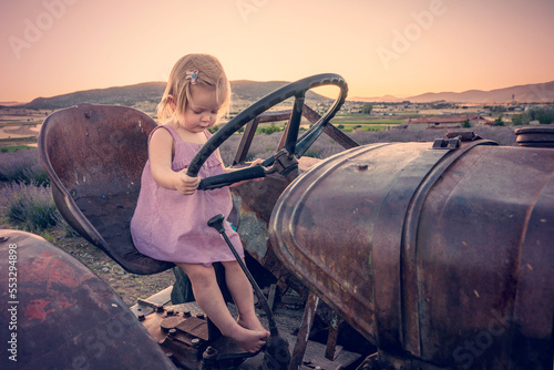 Cute girl on an old tractor. A small child farmer operates agricultural machinery photo