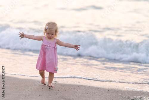 Little girl dancing on the shore. Perfect day at the sea. Toddler in a pink dress plays by the sea. Head is spinning