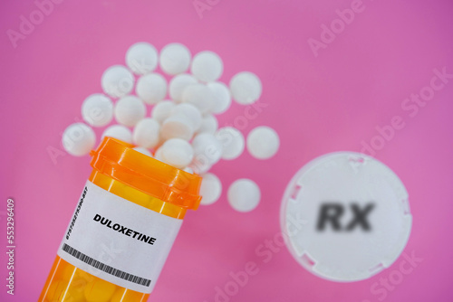 Duloxetine Rx medicine pills in plactic vial with tablets. Pills spilling   from yellow container on pink background. photo